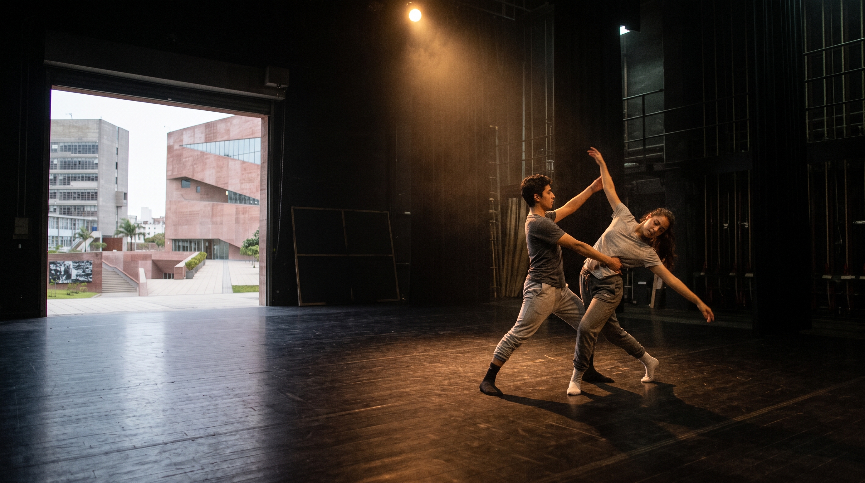 Dos estudiantes ensayando una escena de danza bajo un reflector en un escenario