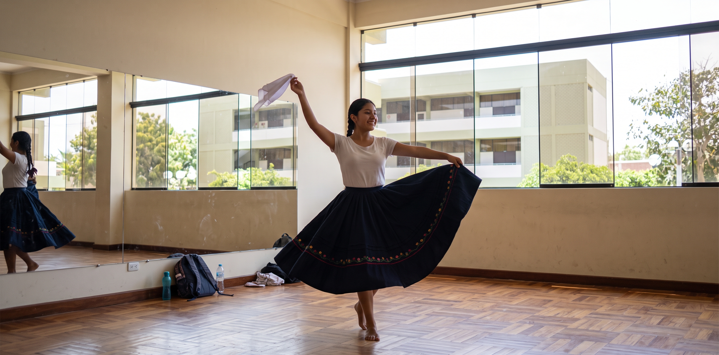 Estudiante de danzas bailando marinera norteña con un pañuelo en la mano, en una sala de ensayo